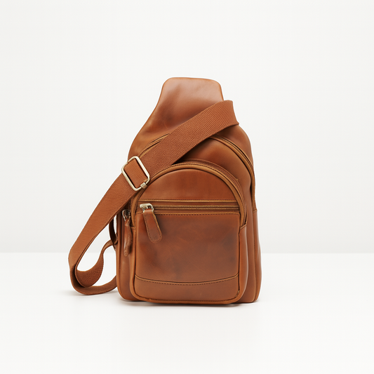 Tan leather crossbody sling backpack with multiple zip compartments and adjustable fabric strap, displayed on white background